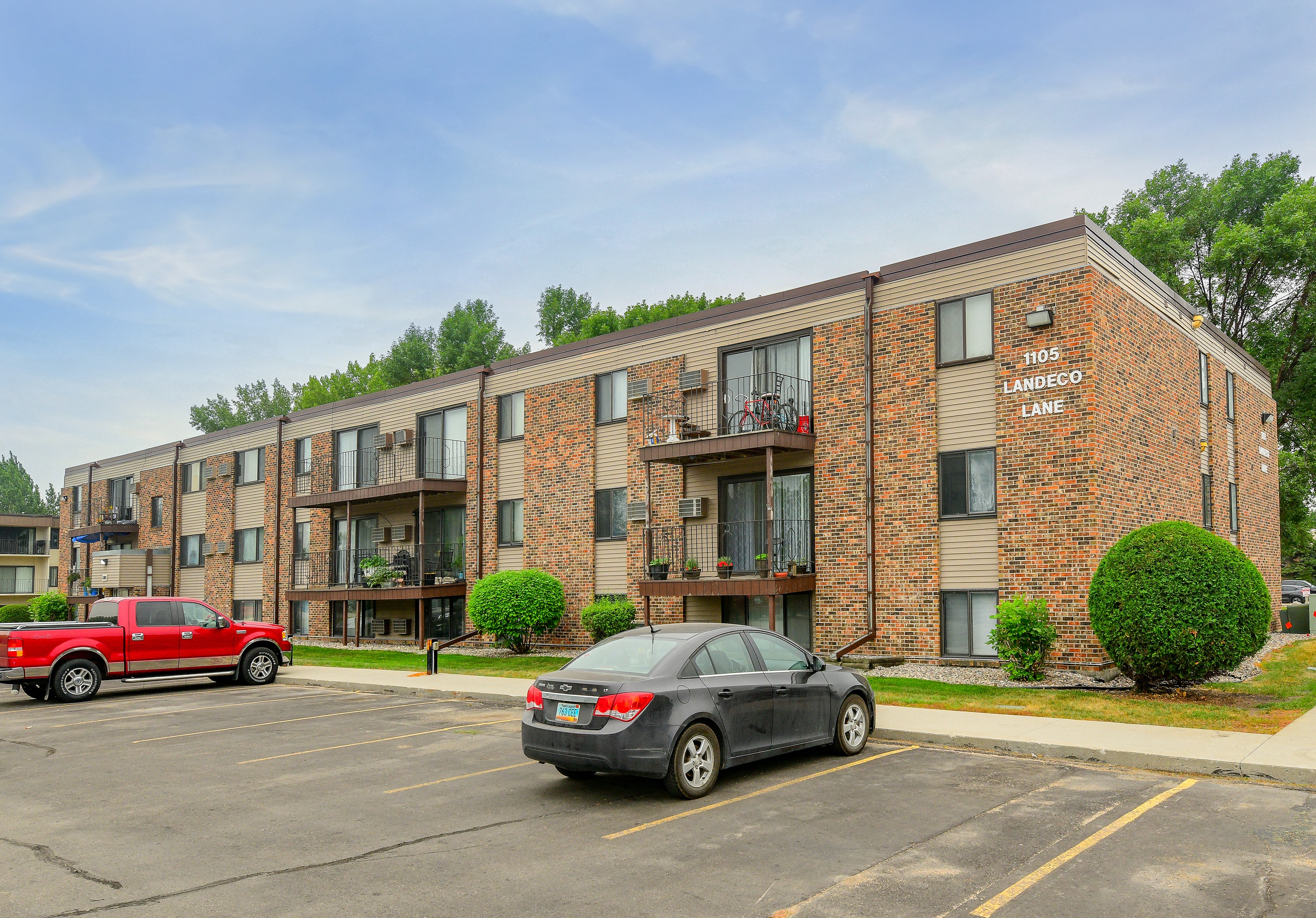 A red truck is parked in front of a brick apartment building.